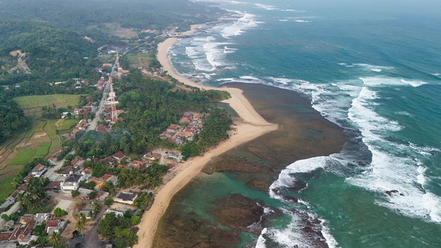 Aerial view of a coastal village with a sandy beach rocky reef and lush palm trees bordering the ocean in Indonesia. Aerial view of a coastal village with a sandy beach rocky reef and lush palm trees bordering the ocean in Indonesia.