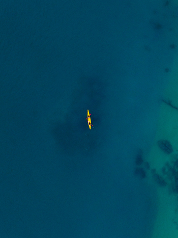 Aerial view of a lone yellow kayak slicing through the turquoise waters near Abel Tasman National Park Tasman Region New Zealand. Aerial view of a lone yellow kayak slicing through the turquoise waters near Abel Tasman National Park Tasman Region New Zealand.