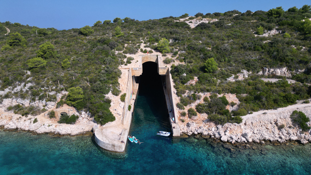 Aerial view of the Yugoslav army underground boat shelter Potkop Parja with people on paddleboards in turquoise water in Rogacic Splitsko dalmatinska Croatia. Aerial view of the Yugoslav army underground boat shelter Potkop Parja with people on paddleboards in turquoise water in Rogacic Splitsko dalmatinska Croatia.