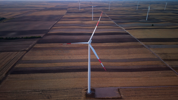 Aerial view of wind turbines standing in vast agricultural fields with striped patterns of harvested land under a soft evening light in Vladimirovac Vojvodina Serbia. Aerial view of wind turbines standing in vast agricultural fields with striped patterns of harvested land under a soft evening light in Vladimirovac Vojvodina Serbia.
