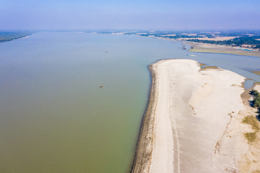 Aerial view of the sandy coastline and calm waters of Kuakata beach with small fishing boats in the sea and lush greenery along the shore in Kuakata Barisal Division Bangladesh. Aerial view of the sandy coastline and calm waters of Kuakata beach with small fishing boats in the sea and lush greenery along the shore in Kuakata Barisal Division Bangladesh.