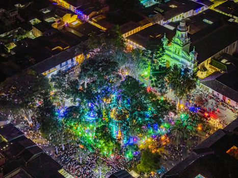 Aerial view of a vibrant town square pulsates with life its trees adorned with glowing lights while the cathedral stands majestically illuminated in green Salamina Caldas Colombia. Aerial view of a vibrant town square pulsates with life its trees adorned with glowing lights while the cathedral stands majestically illuminated in green Salamina Caldas Colombia.