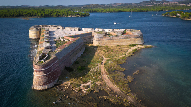 Aerial view of St. Nicholas Fortress a triangular stone fortification surrounded by the blue waters of the Adriatic Sea near green hills in Sibenik Croatia.