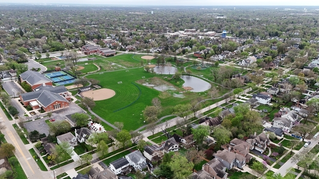 Aerial view of a suburban park featuring baseball diamonds tennis courts and green fields surrounded by residential houses and lush trees in Chicago. Aerial view of a suburban park featuring baseball diamonds tennis courts and green fields surrounded by residential houses and lush trees in Chicago.