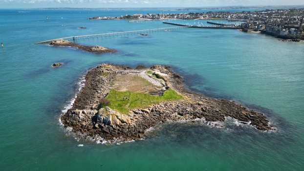 Aerial view of rocky islands surrounded by turquoise waters connected by a long pier stretching towards the distant town Roscoff Brittany France. Aerial view of rocky islands surrounded by turquoise waters connected by a long pier stretching towards the distant town Roscoff Brittany France.