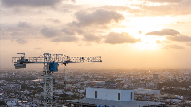Aerial view of a construction crane towering over the urban skyline during a golden sunset with residential buildings and city infrastructure visible in Santo Domingo Dominican Republic. Aerial view of a construction crane towering over the urban skyline during a golden sunset with residential buildings and city infrastructure visible in Santo Domingo Dominican Republic.