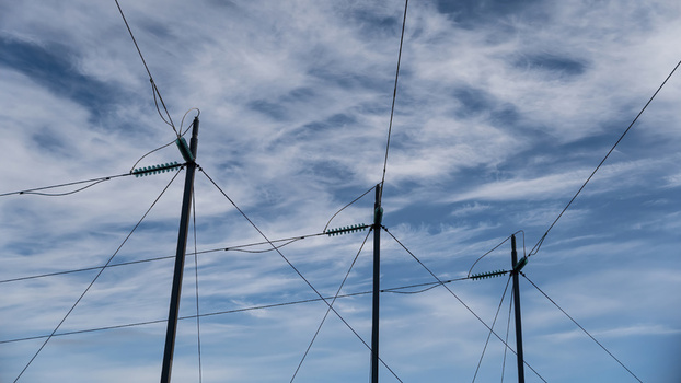 View of high voltage power lines stretching across a blue sky with wispy clouds in Iceland.