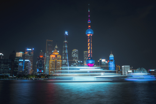 View of the illuminated Lujiazui skyline and the iconic Oriental Pearl Tower at night with light trails from a passing boat on the Huangpu River in Shanghai Shanghai China.