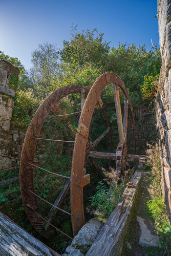 View of a large rusted iron water wheel set within the ruins of a historic stone building in the Tregargus Valley Cornwall United Kingdom. View of a large rusted iron water wheel set within the ruins of a historic stone building in the Tregargus Valley Cornwall United Kingdom.