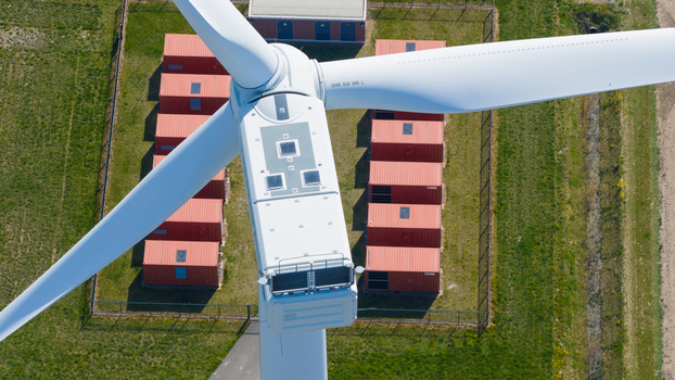 Aerial view of the nacelle and blades of a wind turbine at Energiepark Haringvliet Zuid with rows of red battery storage containers on green grass Middelharnis South Holland Netherlands.