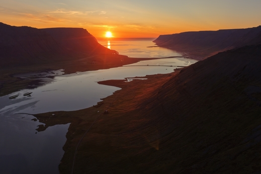 Aerial view of the sunset over the fjord in Flateyri with dramatic mountains and calm water reflecting the golden light Flateyri Isafjardarbaer Iceland. Aerial view of the sunset over the fjord in Flateyri with dramatic mountains and calm water reflecting the golden light Flateyri Isafjardarbaer Iceland.