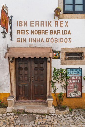 Obidos Portugal 13 May 2026 View of the historic entrance to the Ibn Errik Rex bar with its traditional wooden door and painted signage in the old town. Obidos Portugal 13 May 2026 View of the historic entrance to the Ibn Errik Rex bar with its traditional wooden door and painted signage in the old town.