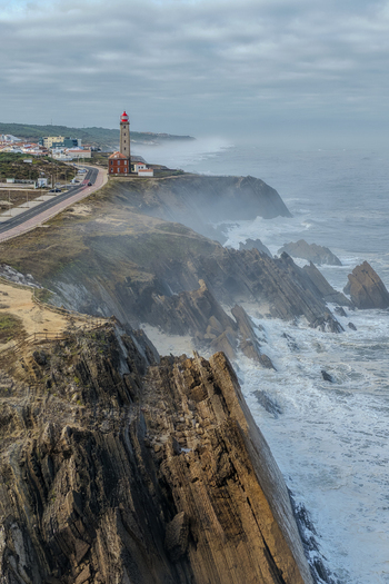 Aerial view of Farol Penedo da Saudade lighthouse standing on rugged cliffs above the crashing waves of the Atlantic Ocean under a misty sky Marinha Grande Leiria Portugal. Aerial view of Farol Penedo da Saudade lighthouse standing on rugged cliffs above the crashing waves of the Atlantic Ocean under a misty sky Marinha Grande Leiria Portugal.