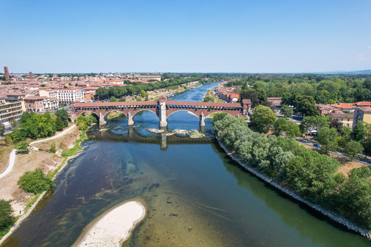 Aerial view of the historic Ponte Coperto bridge spanning the Ticino River with the city skyline and lush green riverbanks under a clear blue sky in Pavia Lombardy Italy. Aerial view of the historic Ponte Coperto bridge spanning the Ticino River with the city skyline and lush green riverbanks under a clear blue sky in Pavia Lombardy Italy.
