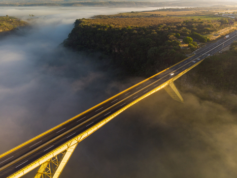 Aerial view of a yellow bridge spanning a deep canyon filled with morning mist under golden hour light in Tonala Jalisco Mexico. Aerial view of a yellow bridge spanning a deep canyon filled with morning mist under golden hour light in Tonala Jalisco Mexico.