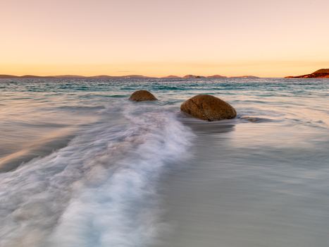 View of Frenchman Bay with waves washing over the sandy shore and two large rocks in the water under a golden sunset sky in Frenchman Bay Western Australia Australia. View of Frenchman Bay with waves washing over the sandy shore and two large rocks in the water under a golden sunset sky in Frenchman Bay Western Australia Australia.