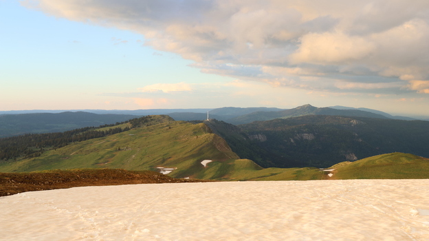 Aerial view of Le Colomby de Gex mountain ridge with green slopes patches of snow and a telecommunications tower under a cloudy sky Echenevex Auvergne Rhone Alpes France. Aerial view of Le Colomby de Gex mountain ridge with green slopes patches of snow and a telecommunications tower under a cloudy sky Echenevex Auvergne Rhone Alpes France.