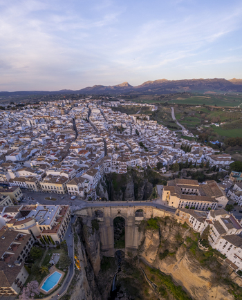 Aerial view of the historic Puente Nuevo bridge spanning the deep El Tajo gorge with white buildings of the old town and distant mountains in Ronda Andalusia Spain. Aerial view of the historic Puente Nuevo bridge spanning the deep El Tajo gorge with white buildings of the old town and distant mountains in Ronda Andalusia Spain.