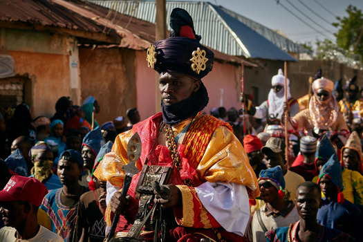 Zaria City Nigeria 22 March 2026 View of a regal figure in opulent red and gold regalia leading a vibrant procession through a bustling street. Zaria City Nigeria 22 March 2026 View of a regal figure in opulent red and gold regalia leading a vibrant procession through a bustling street.