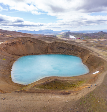 Aerial view of the vibrant turquoise waters of Krafla lake crater surrounded by barren volcanic landscape and distant mountains in Thingeyjarsveit Iceland.