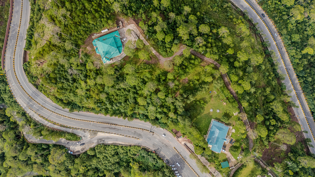 Aerial view of Islamabad Murree Expressway winding through a lush forested landscape with two houses featuring green roofs in Lower Topa Punjab Pakistan. Aerial view of Islamabad Murree Expressway winding through a lush forested landscape with two houses featuring green roofs in Lower Topa Punjab Pakistan.