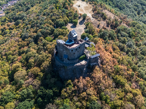Aerial view of Holloko Castle a 13th century medieval stone fortress above forested hills and the historic village in Holloko Hungary during late summer. Aerial view of Holloko Castle a 13th century medieval stone fortress above forested hills and the historic village in Holloko Hungary during late summer.