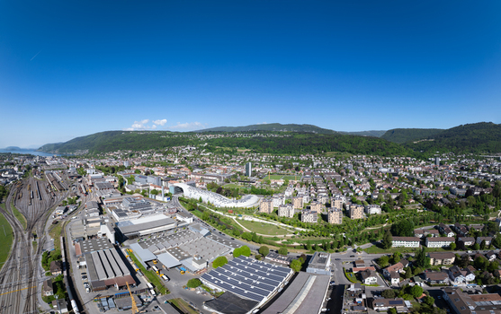 Aerial view of the modern Swatch headquarters and industrial district with railway tracks and green hills under a clear blue sky in Biel Bienne Canton of Bern Switzerland.