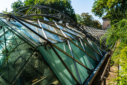 View of a modern glass and steel greenhouse structure with a complex geometric frame surrounded by lush green trees and foliage in a park in Prague Prague Czechia.