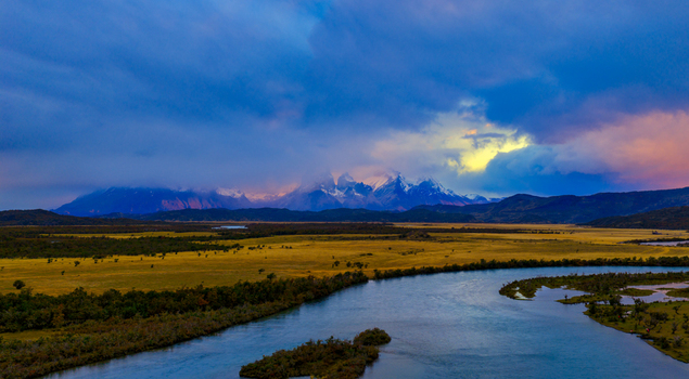 Aerial view of the winding Rio Serrano flowing through golden plains towards the snow capped peaks of Torres del Paine under a dramatic cloudy sky Torres de Paine Magallanes Chile. Aerial view of the winding Rio Serrano flowing through golden plains towards the snow capped peaks of Torres del Paine under a dramatic cloudy sky Torres de Paine Magallanes Chile.