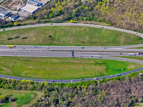 Aerial view of a vibrant highway bisecting verdant fields framed by an oval of lush greenery and scattered trees Sausheim Grand Est France.