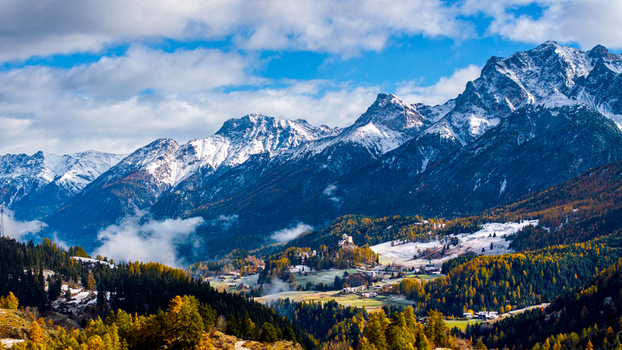 Aerial view of Tarasp Castle on a hill surrounded by autumn forests and snow capped alpine peaks in Scuol Grisons Switzerland.