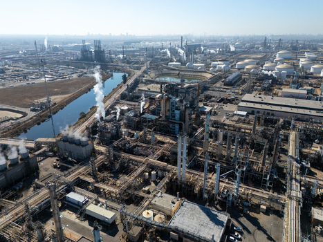 Aerial view of an industrial oil refinery with complex piping systems storage tanks and smoke stacks situated along a canal in Carson California United States.