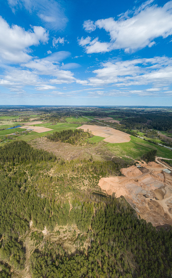 Aerial view of a landscape featuring dense forests agricultural fields and a sand quarry under a bright blue sky in Latvia. Aerial view of a landscape featuring dense forests agricultural fields and a sand quarry under a bright blue sky in Latvia.