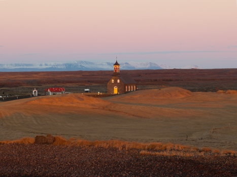 Aerial view of Hvalsneskirkja church set in a vast barren landscape under a soft pink and golden sky in Sudurnesjabaer Iceland. Aerial view of Hvalsneskirkja church set in a vast barren landscape under a soft pink and golden sky in Sudurnesjabaer Iceland.