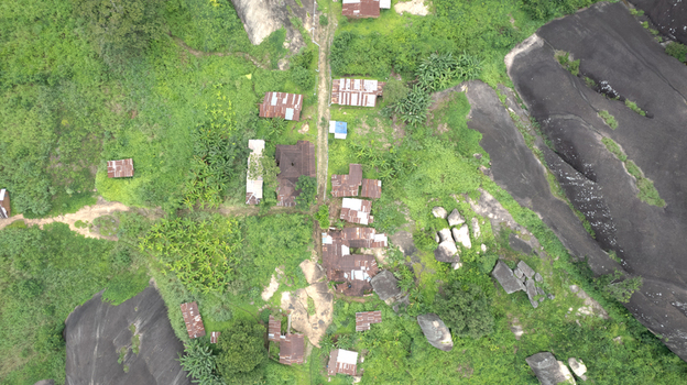 Aerial view of Idanre Hill featuring small houses with corrugated metal roofs nestled among lush green vegetation and large granite rock formations in Idanre Ondo State Nigeria. Aerial view of Idanre Hill featuring small houses with corrugated metal roofs nestled among lush green vegetation and large granite rock formations in Idanre Ondo State Nigeria.