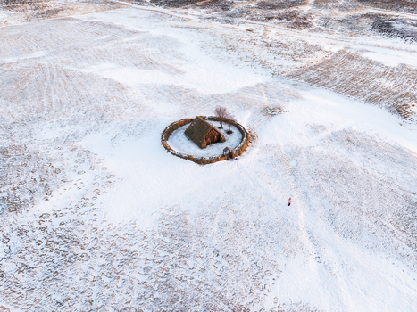 Aerial view of Grafarkirkja a historic turf church enclosed by a circular stone wall in a snow covered landscape with a person walking nearby in Hofsos Skagafjordur Iceland. Aerial view of Grafarkirkja a historic turf church enclosed by a circular stone wall in a snow covered landscape with a person walking nearby in Hofsos Skagafjordur Iceland.