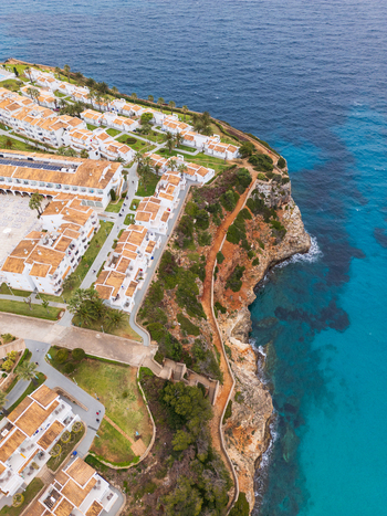Aerial view of Cala Mendia featuring white coastal buildings rugged cliffs and turquoise sea waters in Cala Mendia Illes Balears Spain. Aerial view of Cala Mendia featuring white coastal buildings rugged cliffs and turquoise sea waters in Cala Mendia Illes Balears Spain.