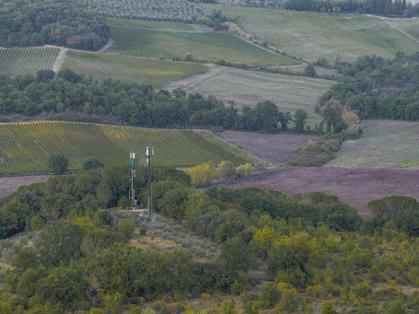 Aerial view of a cell tower situated amidst lush green trees and rolling hills in the countryside of Monteriggioni Tuscany Italy.
