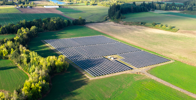 Aerial view of a solar farm with rows of photovoltaic panels situated in a rural agricultural landscape surrounded by green fields and trees in Woodburn Oregon United States. Aerial view of a solar farm with rows of photovoltaic panels situated in a rural agricultural landscape surrounded by green fields and trees in Woodburn Oregon United States.