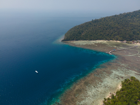Aerial view of Yenbuba jetty extending into the turquoise coral reef waters with a small boat nearby and lush tropical coastline Raja Ampat Southwest Papua Indonesia. Aerial view of Yenbuba jetty extending into the turquoise coral reef waters with a small boat nearby and lush tropical coastline Raja Ampat Southwest Papua Indonesia.