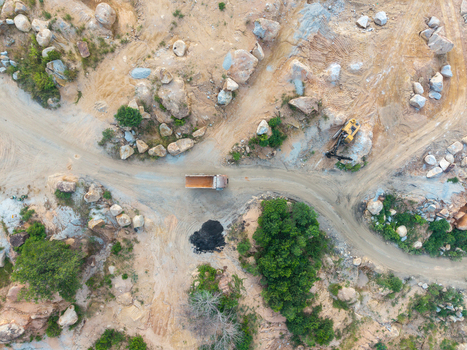 Aerial view of a mining site with a dump truck and excavator operating on rocky terrain surrounded by dirt roads and vegetation in Bukit Tambun Penang Malaysia. Aerial view of a mining site with a dump truck and excavator operating on rocky terrain surrounded by dirt roads and vegetation in Bukit Tambun Penang Malaysia.