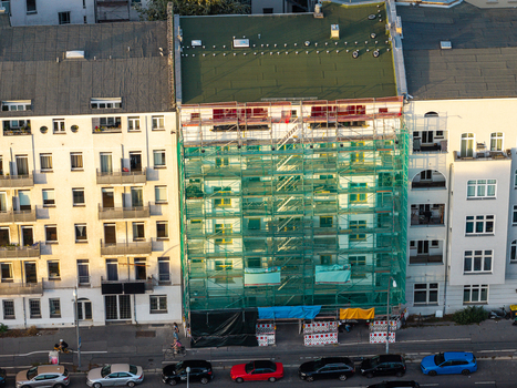Aerial view of a residential building undergoing renovation with green scaffolding and safety netting situated along a city street with parked cars in Berlin Berlin Germany. Aerial view of a residential building undergoing renovation with green scaffolding and safety netting situated along a city street with parked cars in Berlin Berlin Germany.