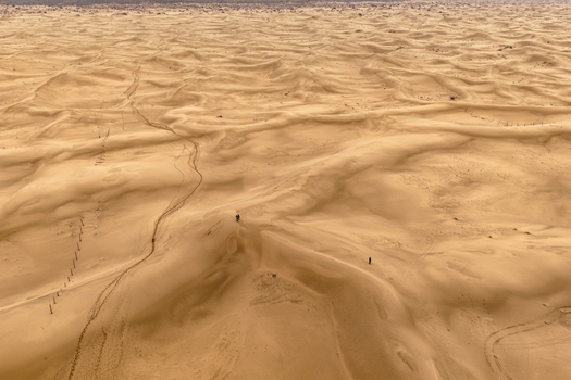 Aerial view of the vast sandy desert with rolling dunes visible tire tracks and two people walking across the landscape in Senek Mangystau Region Kazakhstan.