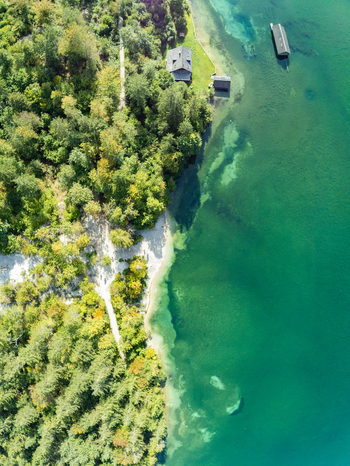 Aerial view of the Attensee lake shore with dense green forest small wooden cabins and clear turquoise water in Rottenbach Bayern Germany. Aerial view of the Attensee lake shore with dense green forest small wooden cabins and clear turquoise water in Rottenbach Bayern Germany.