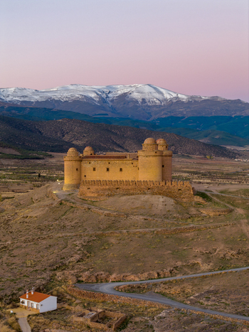 Aerial view of Castillo de La Calahorra a historic castle on a hill with snow capped mountains in the background under a soft sunset sky in La Calahorra Andalucia Spain. Aerial view of Castillo de La Calahorra a historic castle on a hill with snow capped mountains in the background under a soft sunset sky in La Calahorra Andalucia Spain.