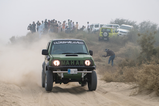 Kot Addu Pakistan 08 November 2024 View of a green off road vehicle racing through the sandy terrain of the Changa Manga Tila Thal Jeep Rally Point with spectators watching in the background.