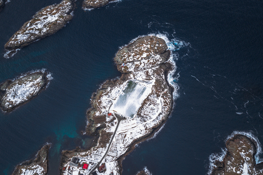 Aerial view of snow dusted islands ringed by dark swirling waters a stark contrast of white and deep blue creating a tranquil yet powerful scene Henningsv&aelig;r Nordland Norway.