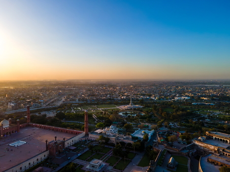 Aerial view of Minar e Pakistan and the historic Badshahi Mosque complex at sunset featuring sprawling gardens intricate architecture and the urban skyline of Lahore Punjab Pakistan.