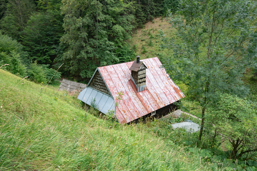 View of a rustic wooden cabin with a weathered red roof nestles on a lush green hillside amidst dense trees Prasnica Velka Fatra Slovakia. View of a rustic wooden cabin with a weathered red roof nestles on a lush green hillside amidst dense trees Prasnica Velka Fatra Slovakia.