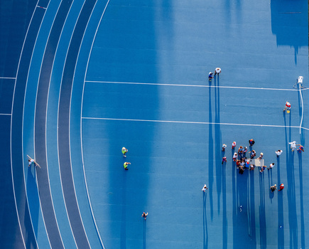 Aerial view of people gathered on a blue running track with white lane markings and long shadows cast by the afternoon sun in Santo Domingo Distrito Nacional Dominican Republic.